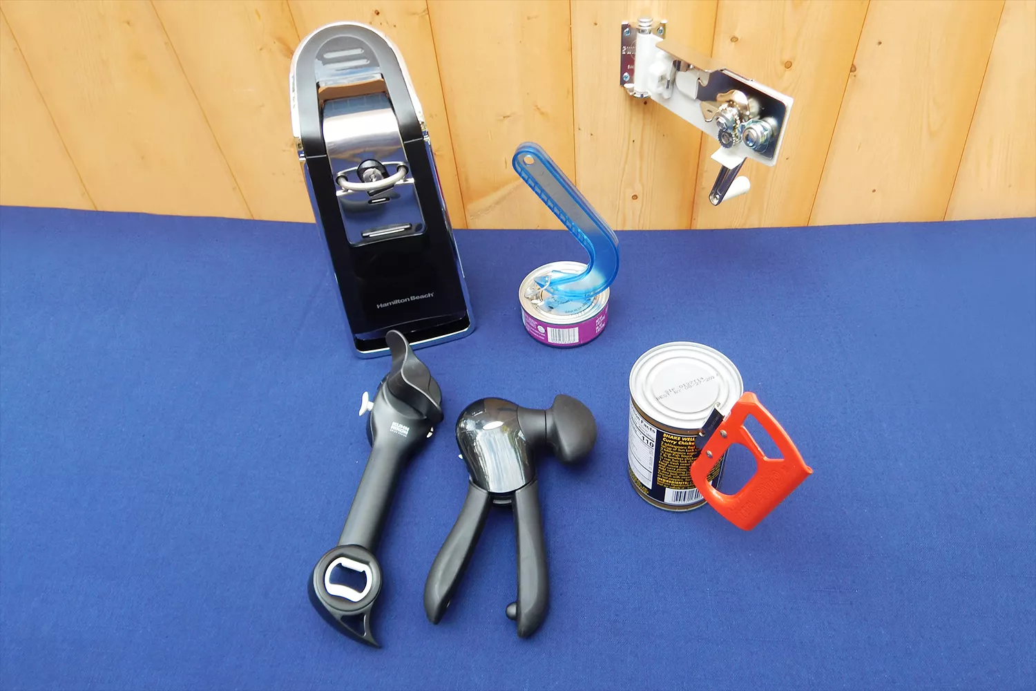 Assortment of can openers we recommend displayed on a blue surface against a wooden background 
